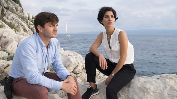 Branka Marić sitzt mit ihrem Kollegen Emil Perica auf einem Felsvorsprung direkt am Meer. Beide schauen in die Ferne. © ARD Degeto/Erika Hauri 