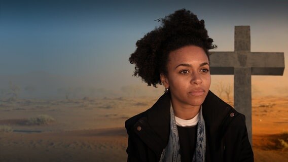 Aminata Belli guckt nachdenklich in die Ferne. Sie steht in Namibia vor einem hölzernen Kreuz. © NDR 