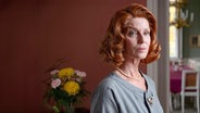 Inge Schaub (Esther Schweins) steht in einem Raum mit dunkler, roter Wand. Auf ihrem Gesicht liegt ein ernster Blick. © NDR/jumpmedientv GmbH/Ulf Thomas 