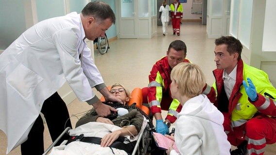 Rosie Pesch (Esther Esche, liegend) wird nach einem Blitzschlag von den Notärzten (Komparsen) in die Sachsenklinik eingeliefert. Als Dr. Kathrin Globisch (Andrea Kathrin Loewig, r.) und Dr. Roland Heilmann (Thomas Rühmann, l.) sie aufnehmen, bleibt ihr Herz stehen. Rosie muss reanimiert werden. © MDR/Peter Krajewsky, honorarfrei 