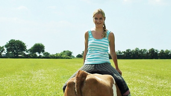 Eine junge Frau sitzt rückwärts auf einer Kuh  