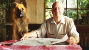Ein Mann sitzt mit seinem Hund an einem Tisch  