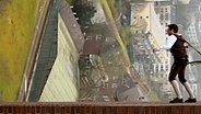 Ein Mann steht mit Seilen gesichert auf einem Haus  