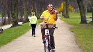 Ein Mann fährt Fahrrad und spielt dabei auf einer Geige  