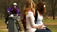 Zwei Frauen sitzen auf einer Bank. Ein Mopedfahrer nähert sich ihnen  