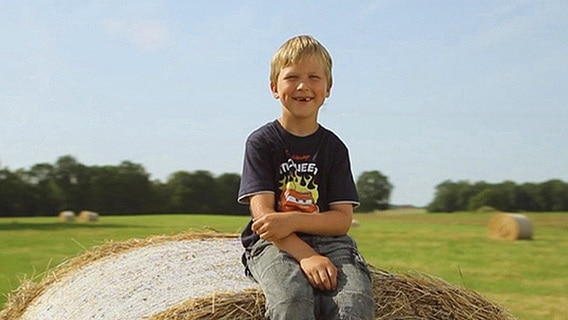 Ein Junge sitzt auf einem Strohballen  