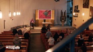 Ein Pfarrer steht vor einer Kirchengemeinde in einer Kirche © NDR 
