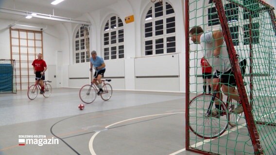 Drei Sportler spielen auf Fährrädern in einer Sporthalle Radball © NDR 