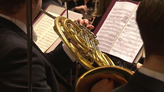 Blick über die Schulter eines Horn-Spielers auf das Instrument und die Noten  