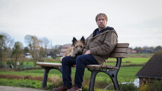 Sørensen (Bjarne Madill) está sentado en un banco con su perro.  © NDR Foto: Michael Ehle