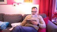 Ein Mann auf dem Sofa mit Tablet in der Hand.  