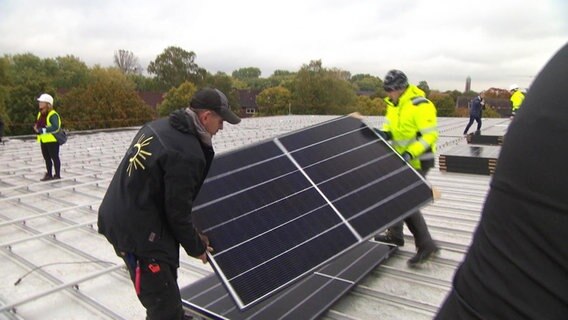 Zwei Männer bringen eine Solaranlage auf ein Dach an.  