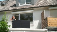Eine Frau reinigt ein Solar-Panel an einem Balkon. © NDR 