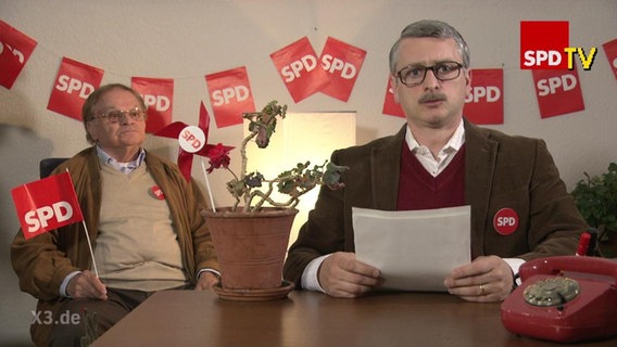Zwei Männer umgeben von SPD-Fähnchen.  