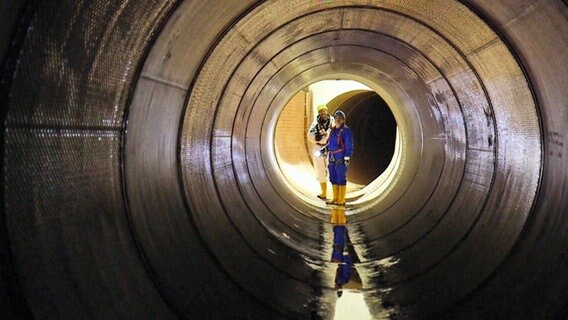 Blick in einen Tunnel der Hamburger Kanalisation. Am Ende des Tunnels stehen zwei Männer - ein Kanalarbeiter und der Filmemacher Timo Großpietsch. © NDR 