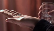 Eine Hand mit zwei kleinen Tabletten. © NDR/Kulturjournal 