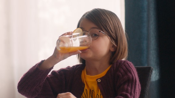 Szenenbild aus der französischen Serie "Ziemlich beste Stiefmutter": Ein junges Mädchen mit Brille trinkt ein Glas Orangensaft. © The Film TV 