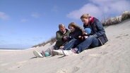 Familie Zimmermann sitzt im Sand in den Dünen  