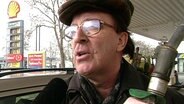 Mann an einer Tankstelle mit Zapfhahn in der Hand.  