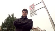 junger Mann mit verschränkten Armen vor Tempo-30-Schild  