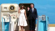 Melania und Donald Trump winken von der Flugzeugtreppe.  