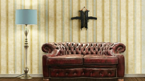 Ein Kreuz aus zwei Schusswaffen hängt hinter einem Sofa an der Wand.  