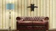 Ein Kreuz aus zwei Schusswaffen hängt hinter einem Sofa an der Wand.  
