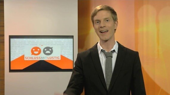 Ein Moderator im Studio lächelt in die Kamera.  