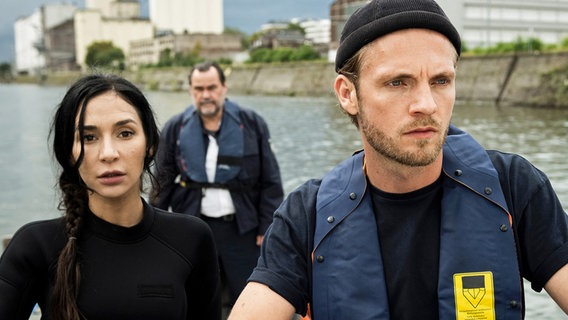 Gerade erst hat Arda Turan (Yasemin Cetinkaya, l.), ehemals Hochleistungsschwimmerin, ihren Dienst bei der Wasserschutzpolizei Duisburg angetreten. Mit Gerhard Jäger (Markus John, h.) und Frank van Dijk (Niklas Osterloh, r.) verfolgen sie ein Boot im Duisburger Hafen. © ARD/Laurent Trümper 