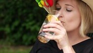 Eine Frau trinkt aus einem Wasserglas.  