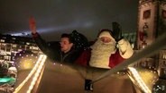 Ein Mann sitzt neben einem Weihnachtsmann in einer Kutsche über dem Hamburger Rathaus.  