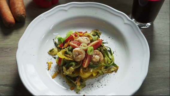 Ein Teller Gemüsespaghetti mit Garnelen steht auf dem Tisch, daneben ein Glas Rote-Bete-Saft. © Screenshot 