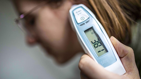 Bei einer jungen Frau wird mit einem digitalen Messgerät Fieber gemessen. © imago images / photothek Foto: Florian Gaertner