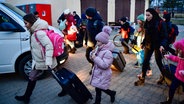 Geflüchtete Frauen und Kinder mit Rollkoffern überqueren einen Parkplatz © picture alliance/dpa Foto: Marton Monus