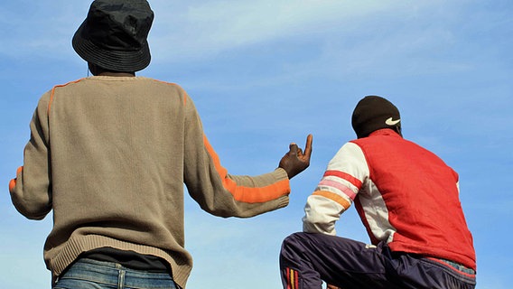 Zwei afrikanische Flüchtlinge von hinten fotografiert, im Hintergrund blauer Himmel. © Alexander Göbel 