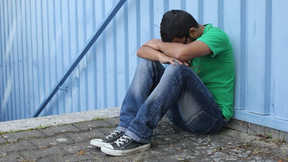 Ein junger Mann sitz mit angezogenen Beinen und aufgestütztem Kopf auf dem Boden vor einer Treppe. © fotolia.com Foto: shootingankauf