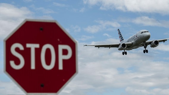Ein Flugzeug am Himmel, im Vordergrund ist ein Stoppzeichen unscharf zu sehen. © picture alliance Foto: Photoshot
