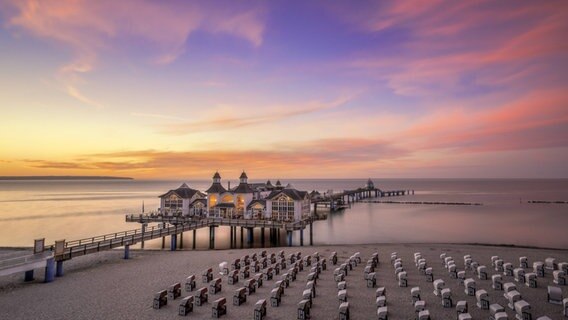 Die Seebrücke Sellin in Rügen beleuchtet im Sonnenuntergang mit ordentlich aufgereihten Strandkörben im Vordergrund. © imago images / Photocase Foto: Photocase