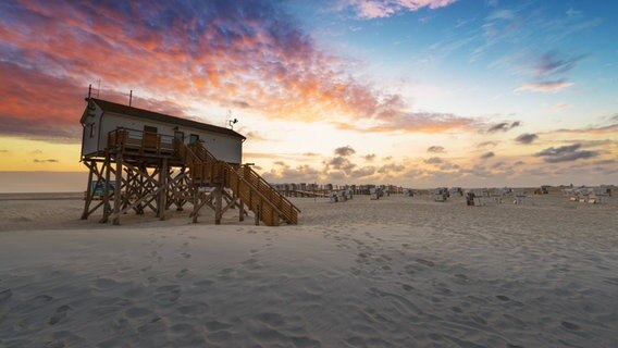 Pfahlbauten am Strand in Sankt Peter-Ording im Sonnenuntergang. © imago images / Westend61 