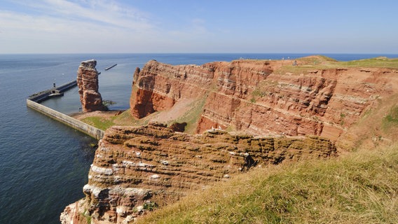 Die rote Steinküste auf Helgoland mit Meerblick und vor blauem Himmel. © picture alliance/imageBROKER 