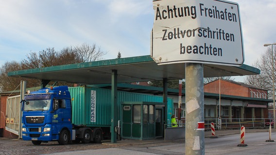 An einer Laterne hängt das Schild: "Achtung Freihafen, Zollvorschriften beachten". Dahinter hält ein Lkw an der Zollstation am Ernst-August-Kanal. © NDR Foto: Daniel Sprenger