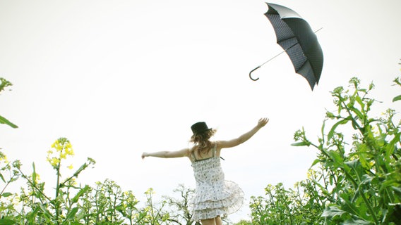 Eine junge Frau in einem Sommerkleid läuft durch ein Feld und wirft einen Regenschirm in die Luft. © photocase.de Foto: Cattari Pons