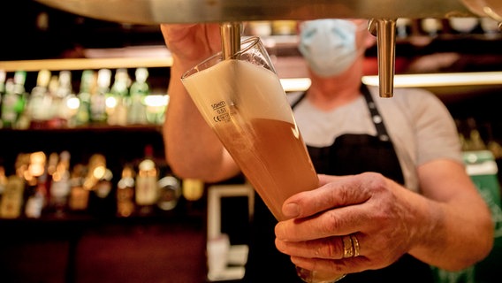 Ein Wirt mit Maske zapft in einer Kneipe Bier. © picture-allaince Foto: Christoph Soeder
