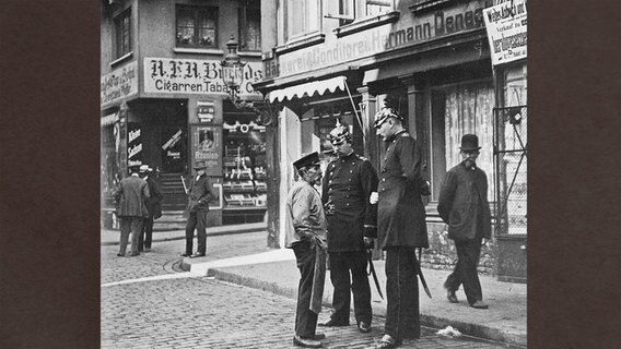 Im Hamburger Gängeviertel der Altstadt wird ein Mann von zwei Polizisten kontrolliert. © Denkmalschutzamt Hamburg Bildarchiv 