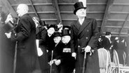 Winston Churchill bei der Eröffnung des Festival of Britain, London, 1951. Sitzen Sie ganz in der Mitte des Fotos, mit einem Zylinder und zahlreichen Medaillen, Orden und Ehrenzeichen. Rechts von ihm steht Premierminister Clement Attlee. © picture-alliance / HIP | Museum von London 