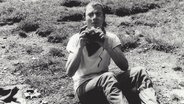 Schwaz-weiß-Foto: Ein Mann sitzt auf einer Wiese, einen Fotoapparat in der Hand.  