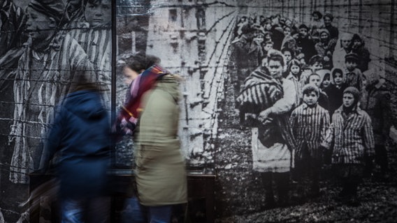 zwei junge Menschen bewegen sich vor einem historischen KZ-Bild © NDR/ Foto: Christian Spielmann