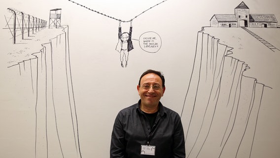 Der Cartoonist Michel Kichka steht unter seiner Wandzeichnung in der Bibliothek des Krakauer Mocaks. © NDR Foto: Judith Pape