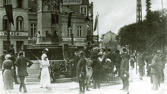 Schwarz-weiß-Foto: Menschen vor dem John-Brinckman-Brunnen in Rostock.  