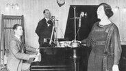Olive Sturgess and John Huntingdon treten bei einem BBC-Konzert auf. Es ist eine Szene aus den frühen Sendetagen der BBC im Jahr 1922. © picture alliance / Mary Evans Picture Library 